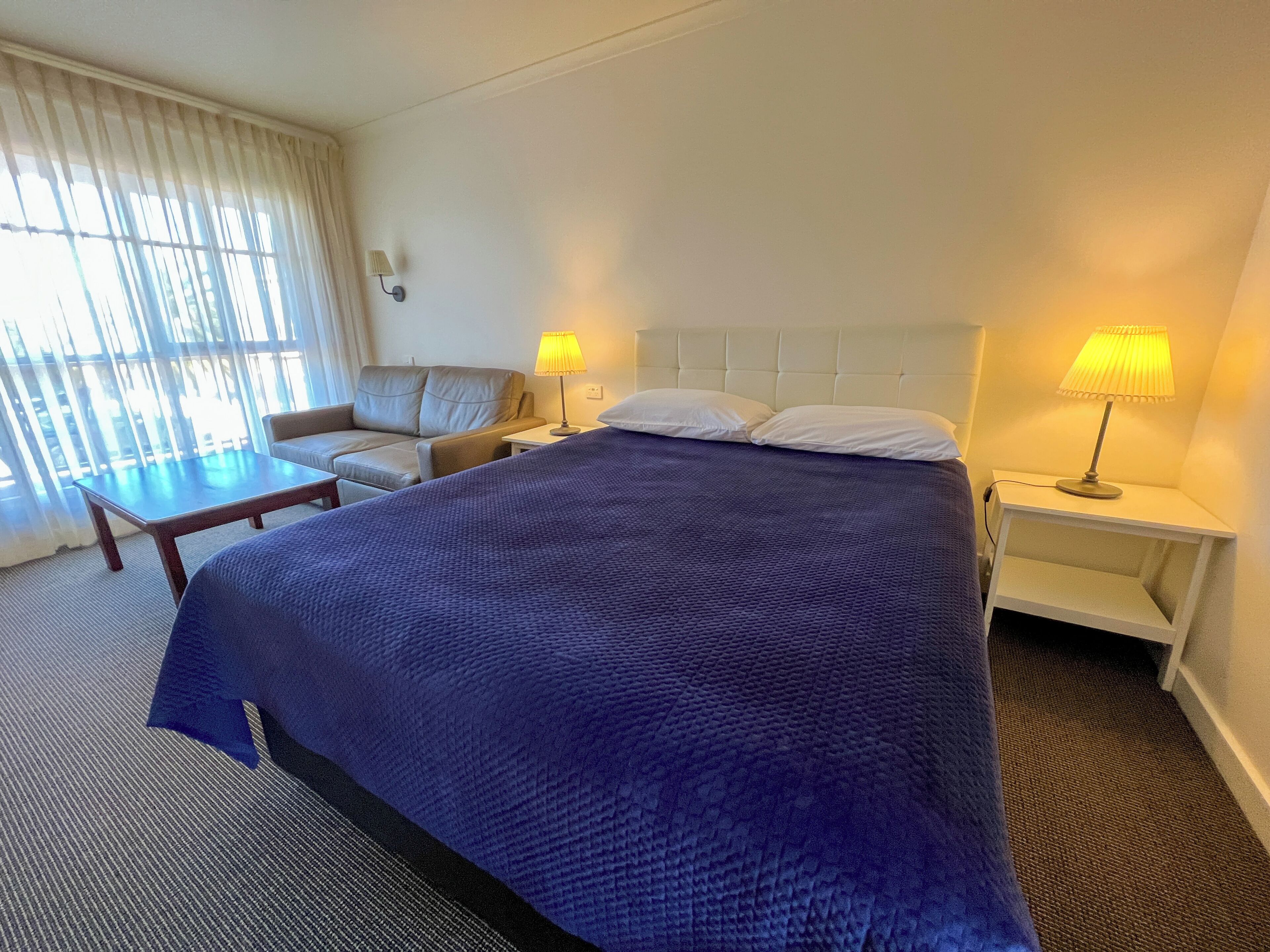Une chambre d’hôtel avec un grand lit, un canapé, une petite table, deux lampes de chevet et une fenêtre avec des rideaux.