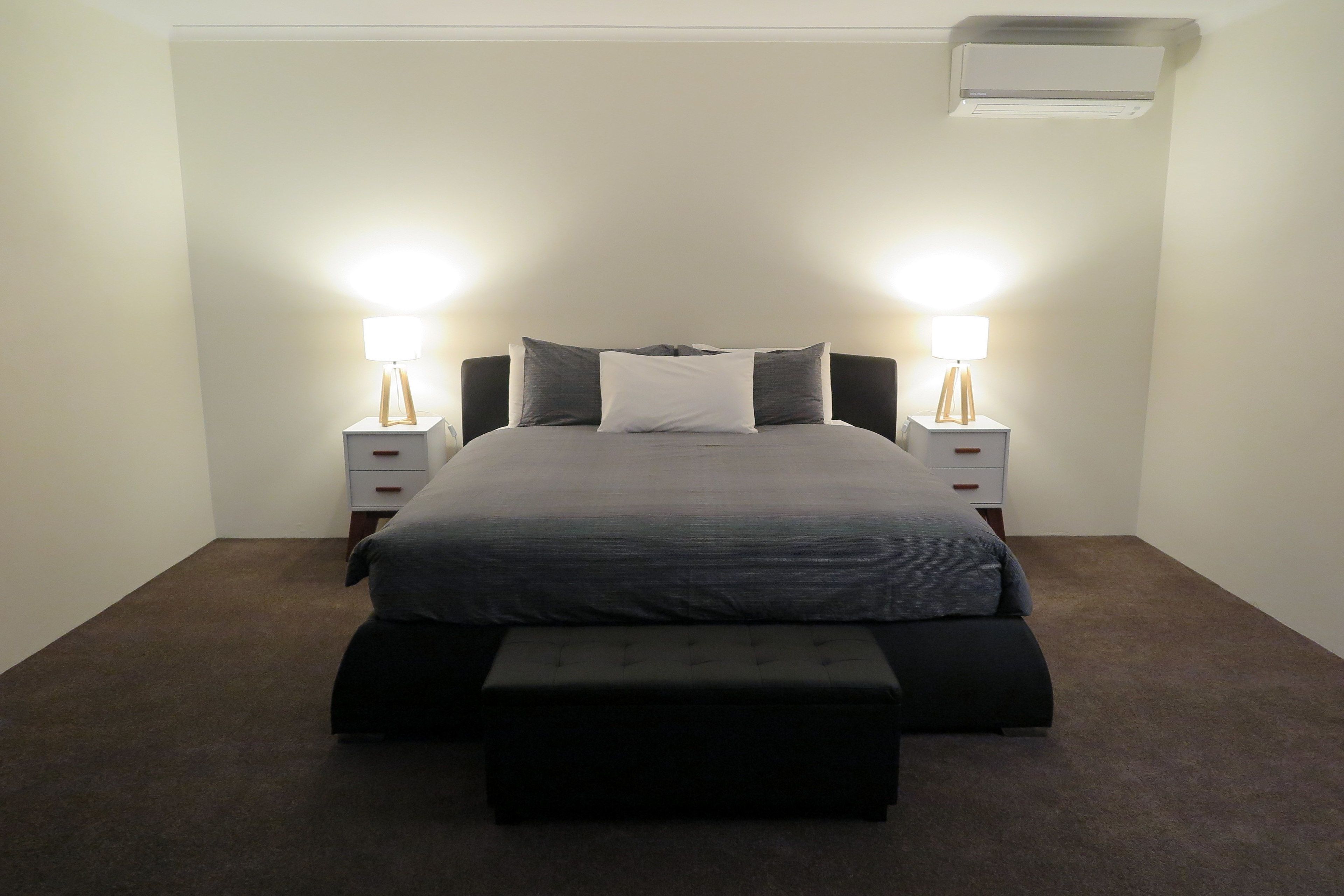 Un dormitorio ordenado con cama, mesitas de noche y un banco.
