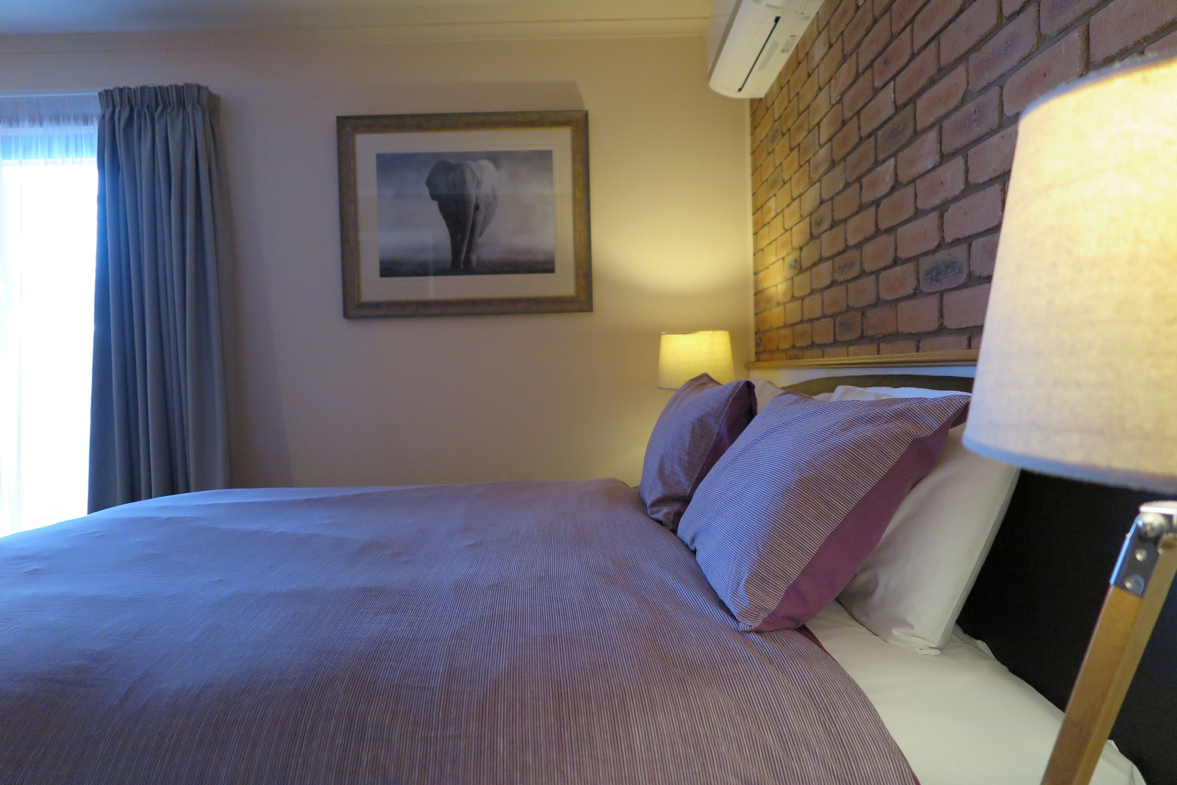 Quarto de hotel com uma cama grande, um quadro na parede, uma luminária e uma parede de tijolos.