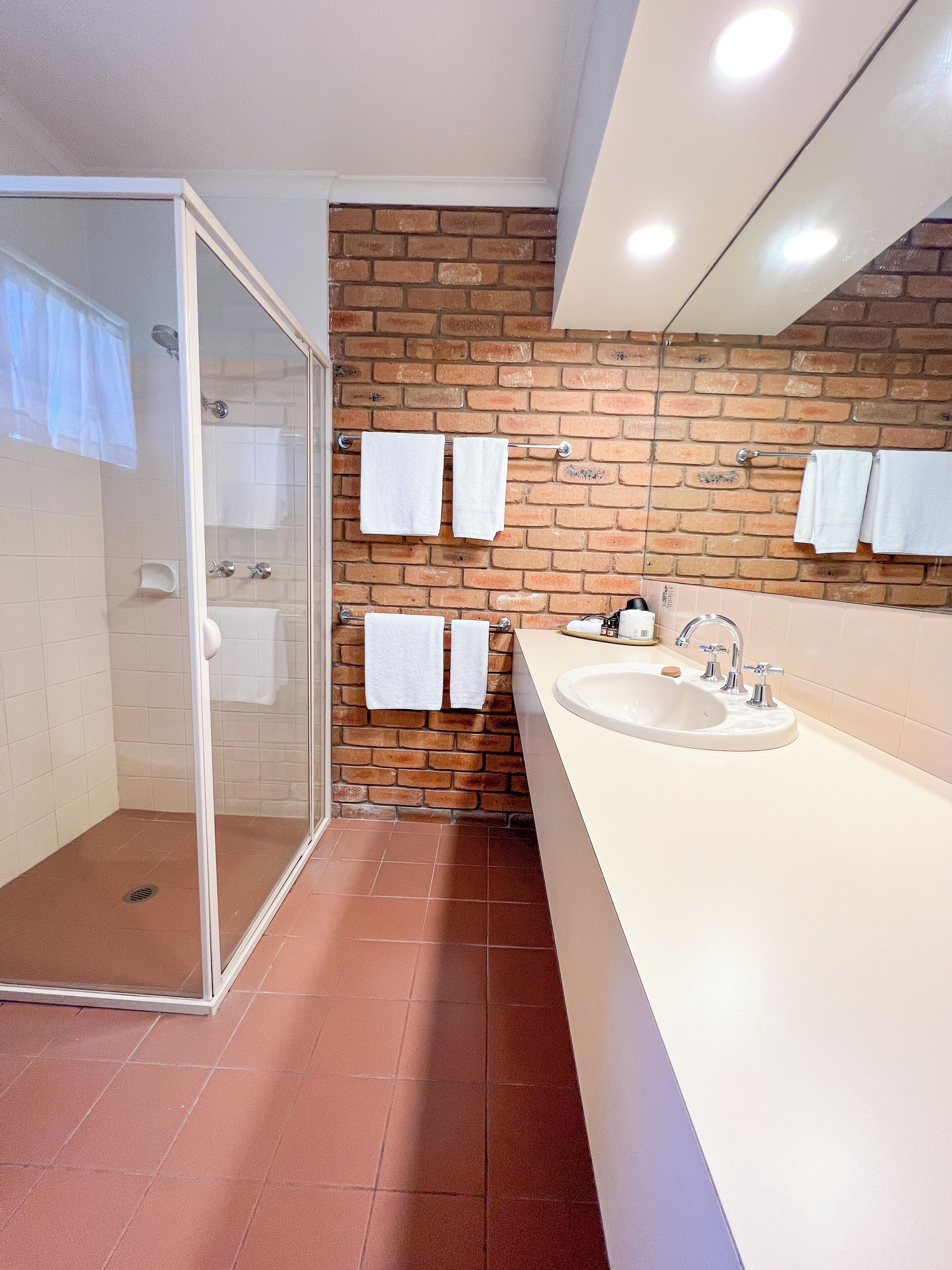Un baño con cabina de ducha de vidrio, un lavamanos con espejo y una pared de ladrillo.