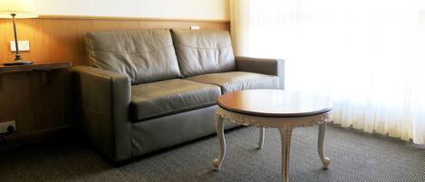A room with a grey leather sofa, a small round table, a lamp, and a wall-mounted light fixture.