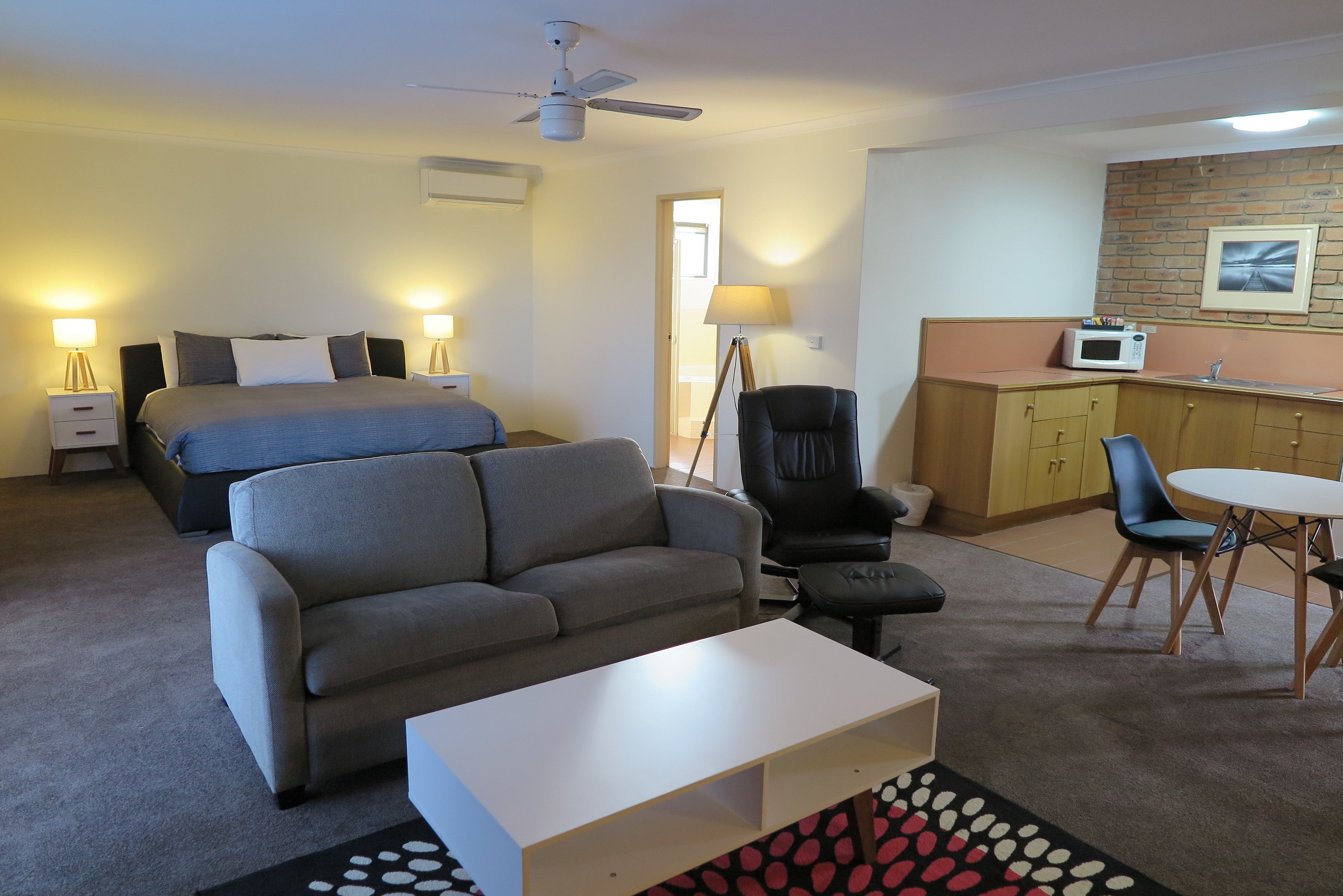 A hotel room with a bed, a sofa, a desk, a chair, a dining table, and a microwave.