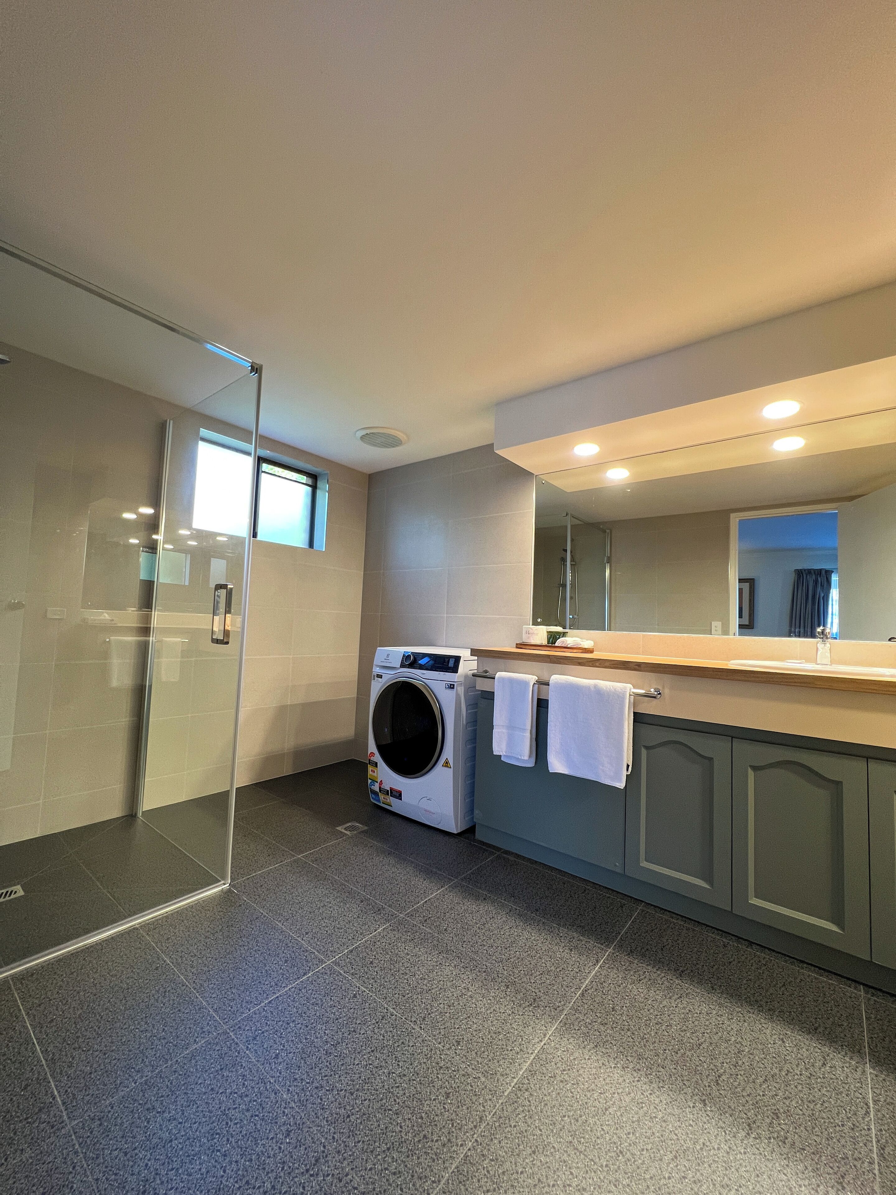 A modern bathroom with a glass shower enclosure, a built-in washing machine, and a large mirror above the sink.