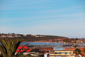 A coastal town with a marina, buildings with red roofs, and a hilly backdrop.