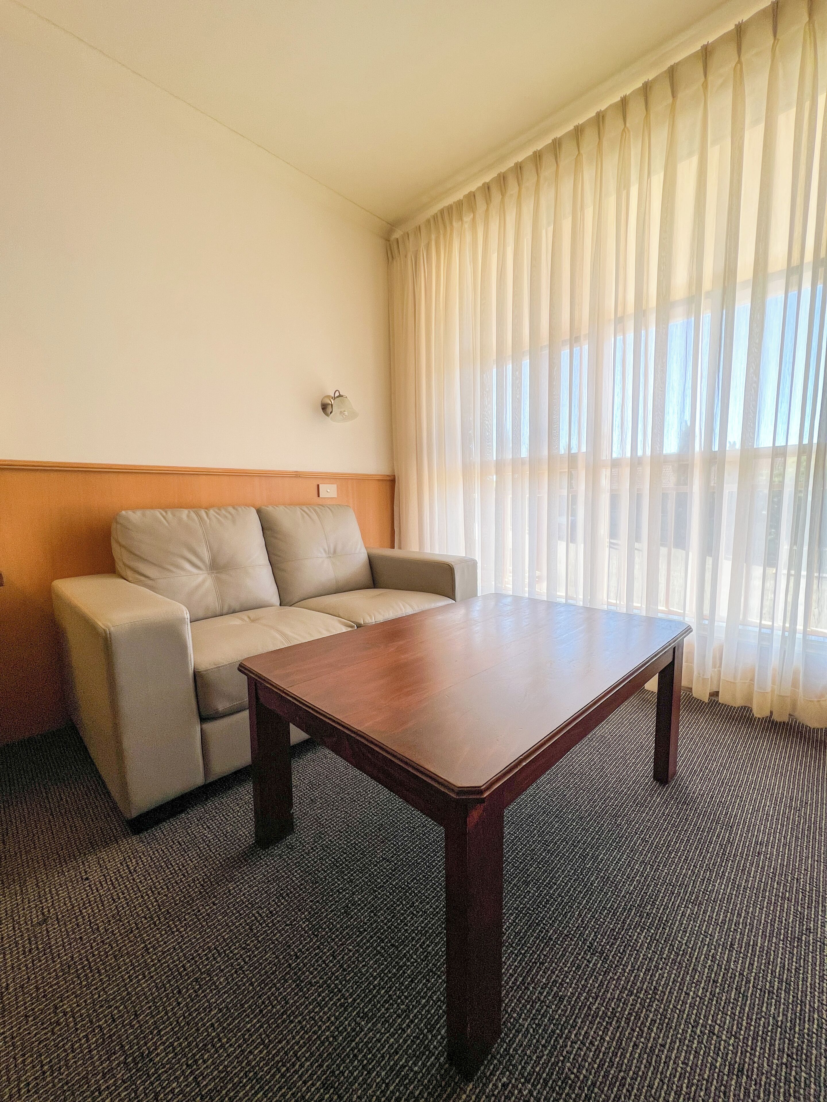 Una habitación de hotel con sofá, una mesa de madera y cortinas ligeras.