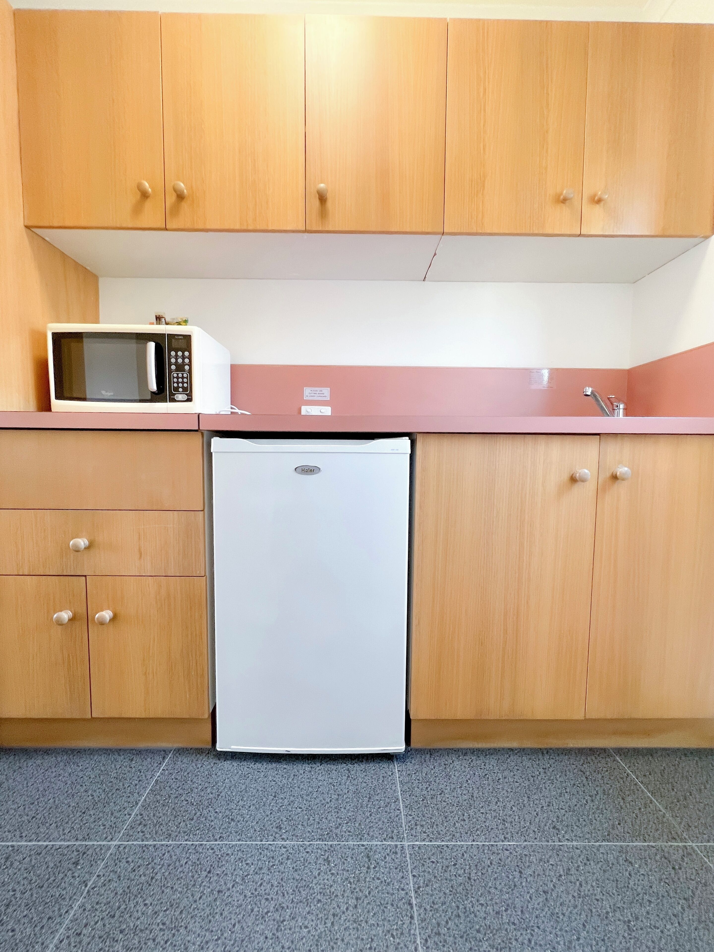 A compact kitchen with wooden cabinets, a white refrigerator, and a microwave on the countertop.
