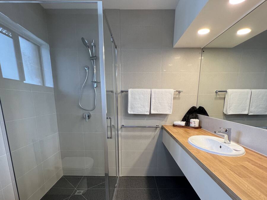 A modern bathroom with a glass-enclosed shower, a white sink, and a large mirror.