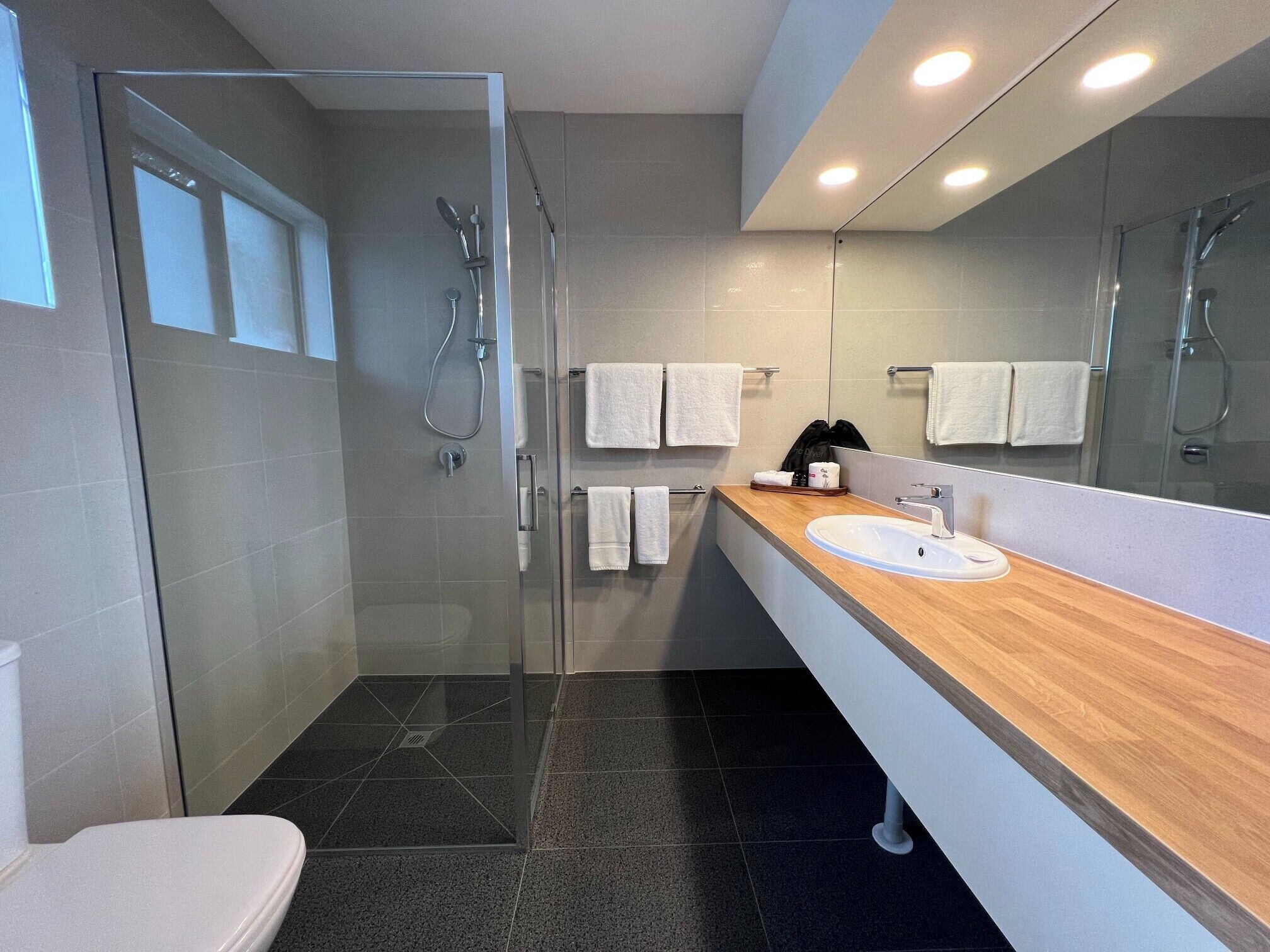A modern bathroom with a glass-enclosed shower, a wooden vanity with a sink, and a large mirror.