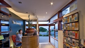 Un área de recepción con un mostrador, un jarrón grande y una estantería con libros de viajes.