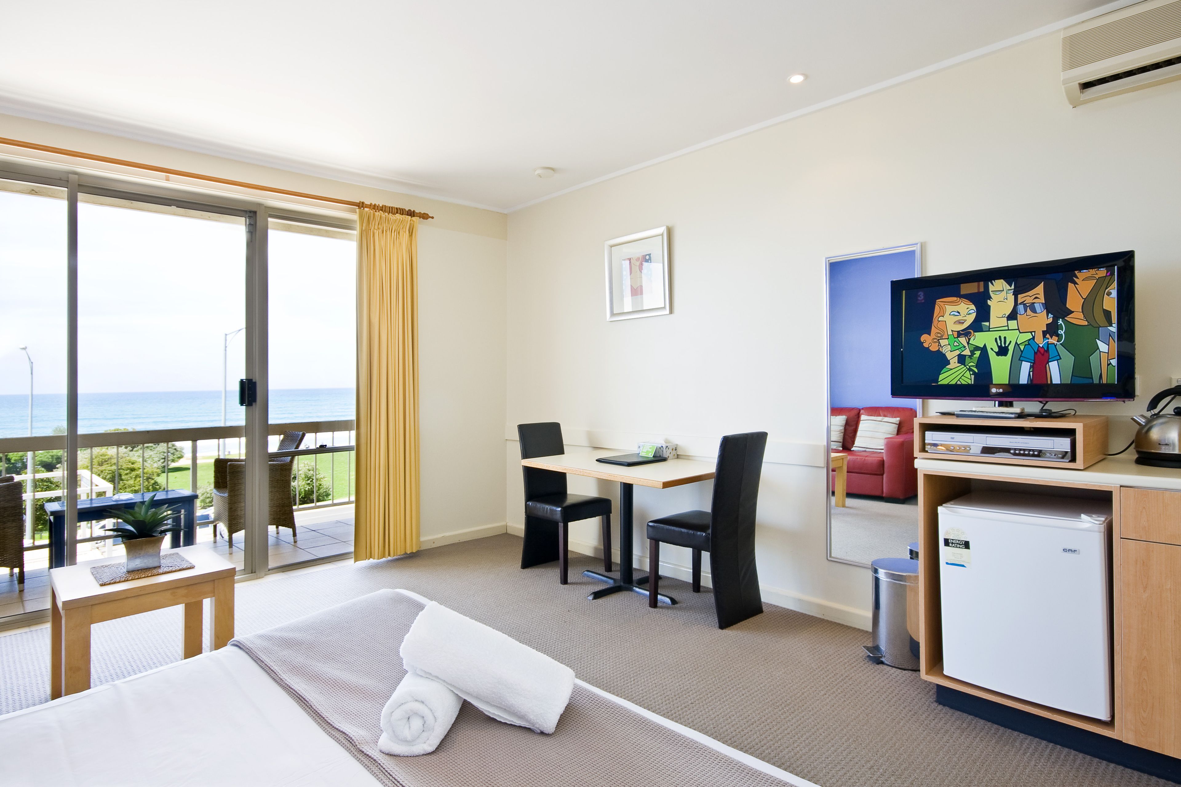 Ett hotellrum med en säng, ett skrivbord, en stol, en tv och utsikt över havet.