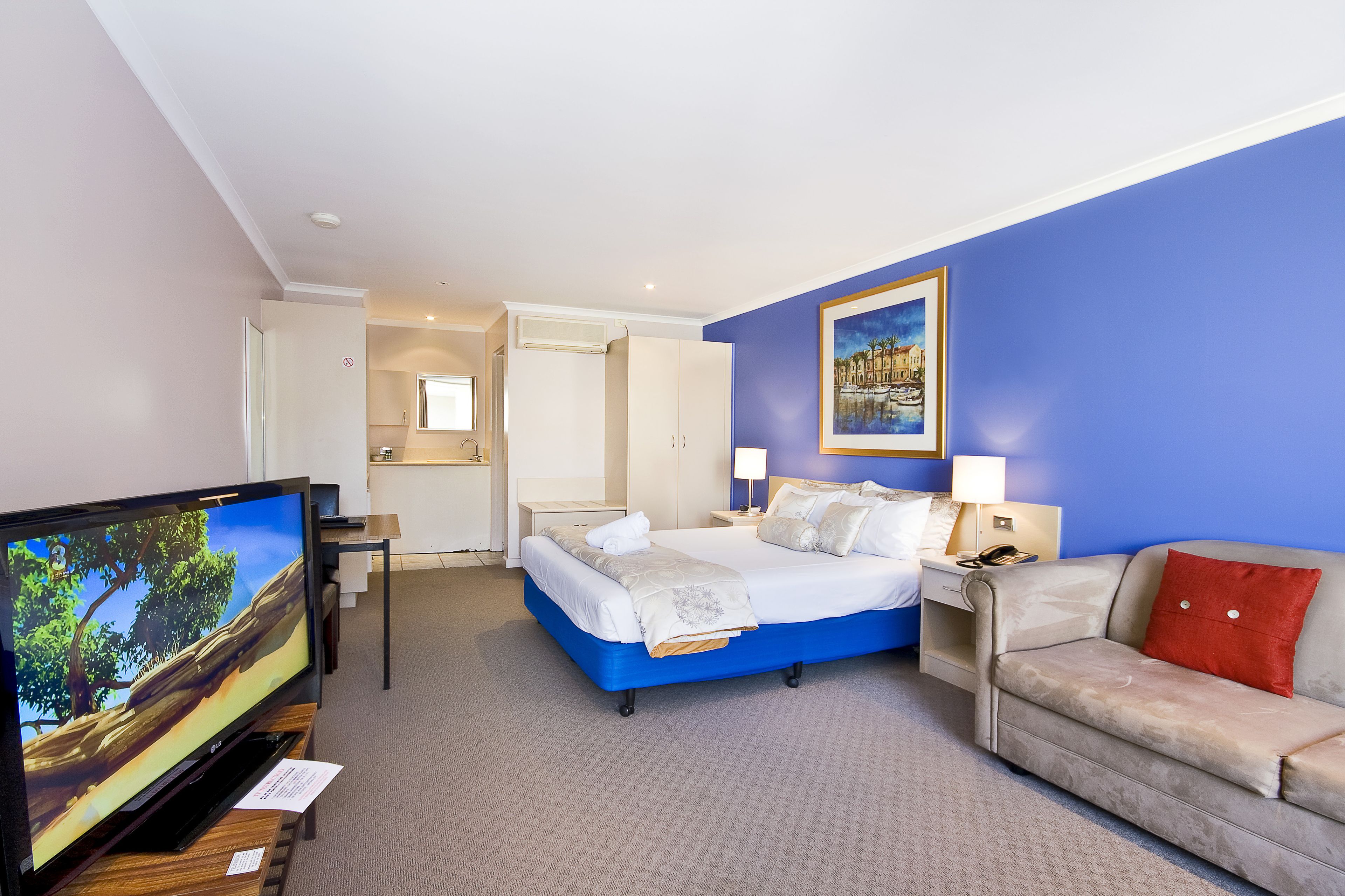 Una camera d'albergo con un letto, una TV, un divano e un quadro appeso al muro.