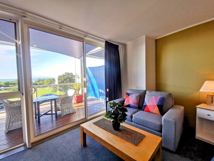 A modern living room with a sofa, a coffee table, and a view of the outdoors through large sliding glass doors.