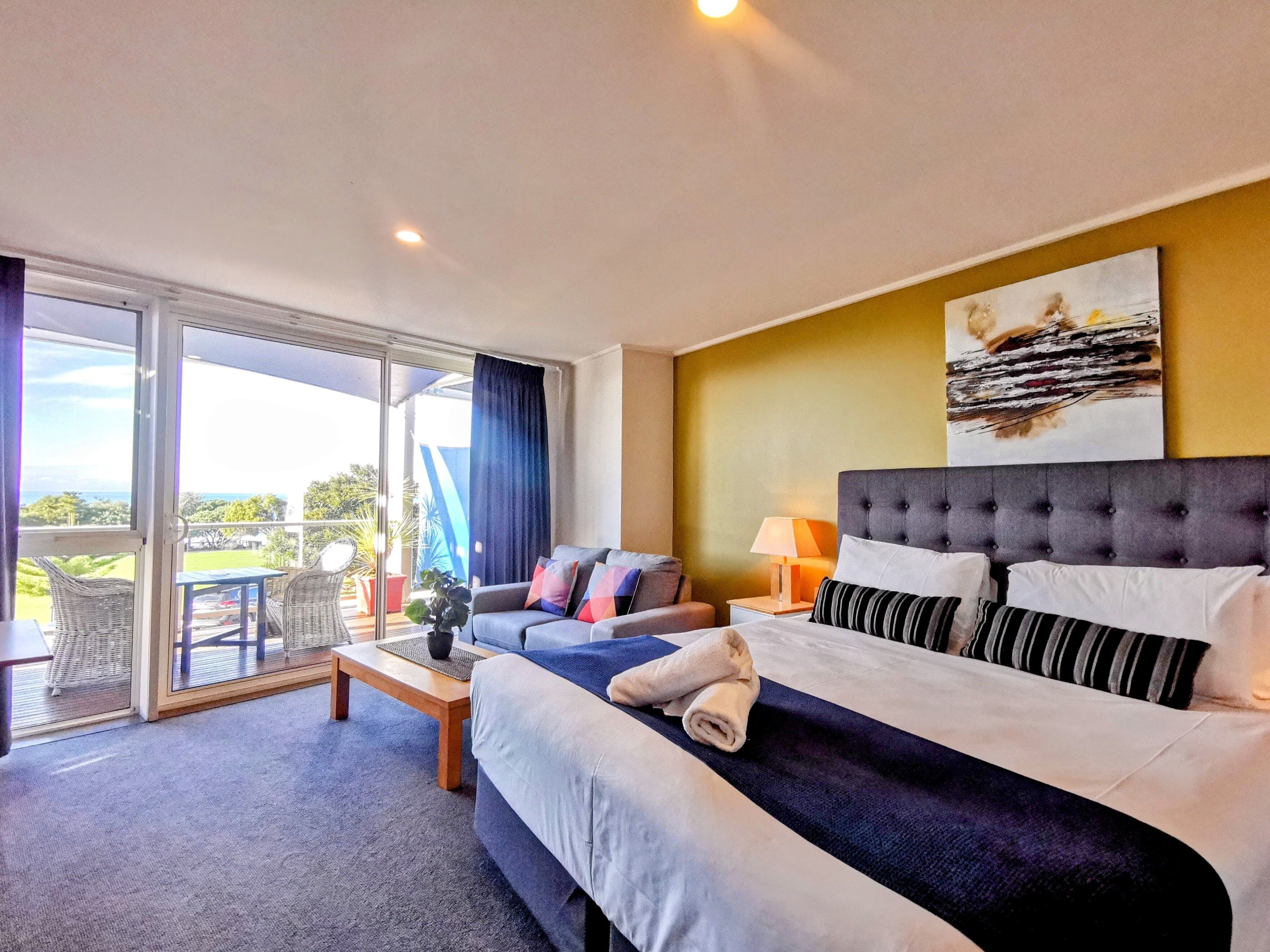 A hotel room with a bed, a sofa, a table, and a balcony with a view.