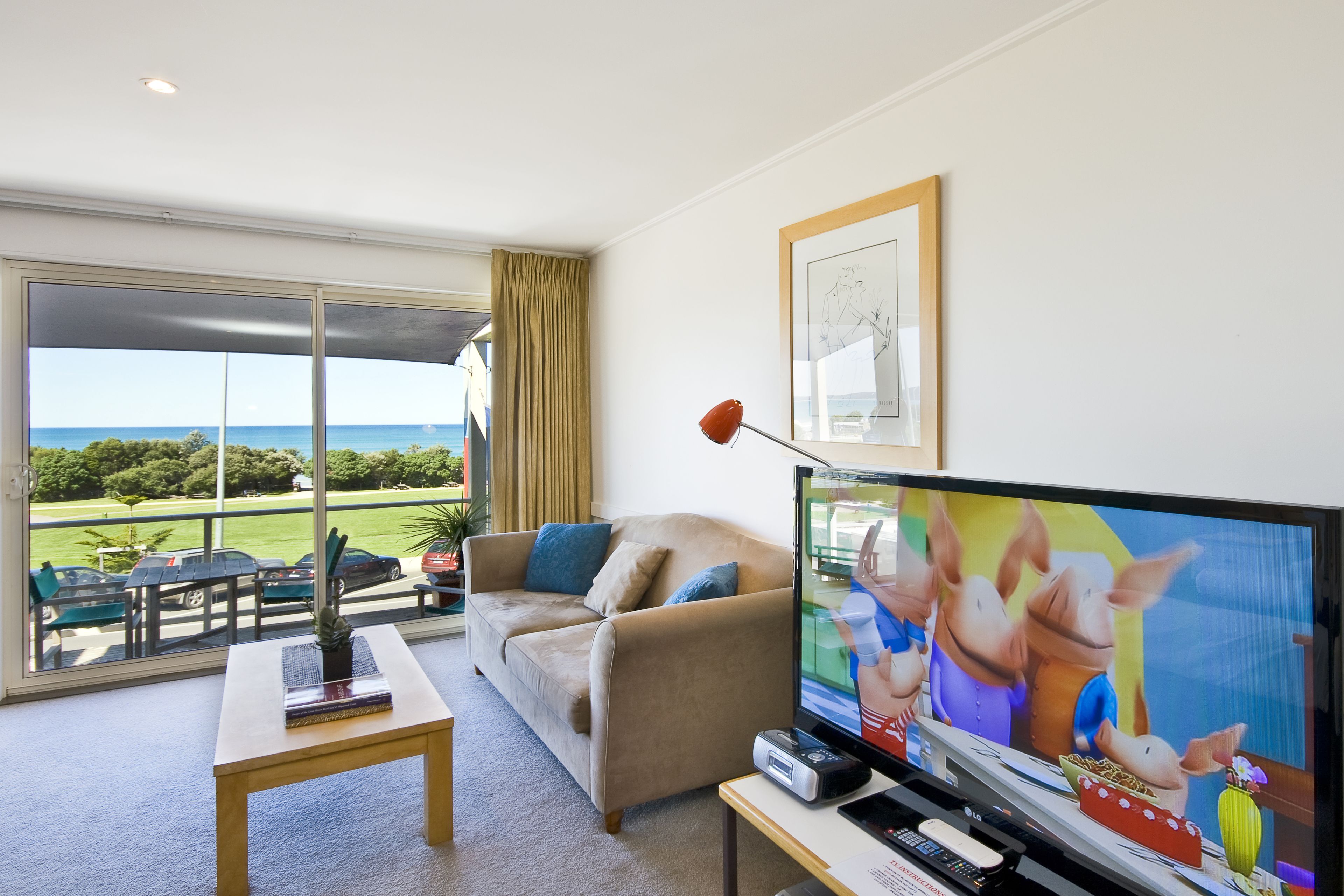 A living room with a large TV, a sofa, a coffee table, and a view of the outdoors.