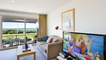 A living room with a large TV, a sofa, a coffee table, and a view of the outdoors.