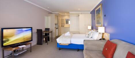 A hotel room with a bed, a sofa, a TV, a desk, and a bathroom visible in the background.