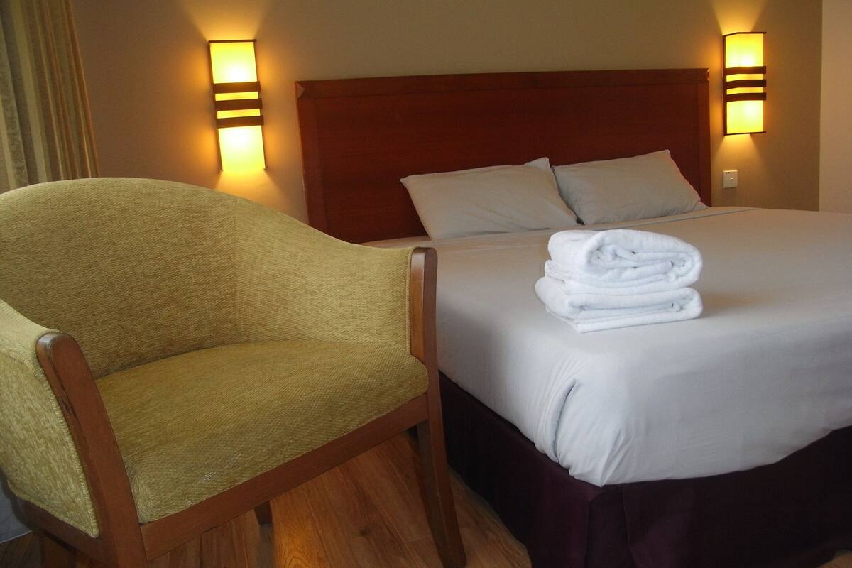 Une chambre d’hôtel avec un lit, une chaise et deux lampes fixées au mur.