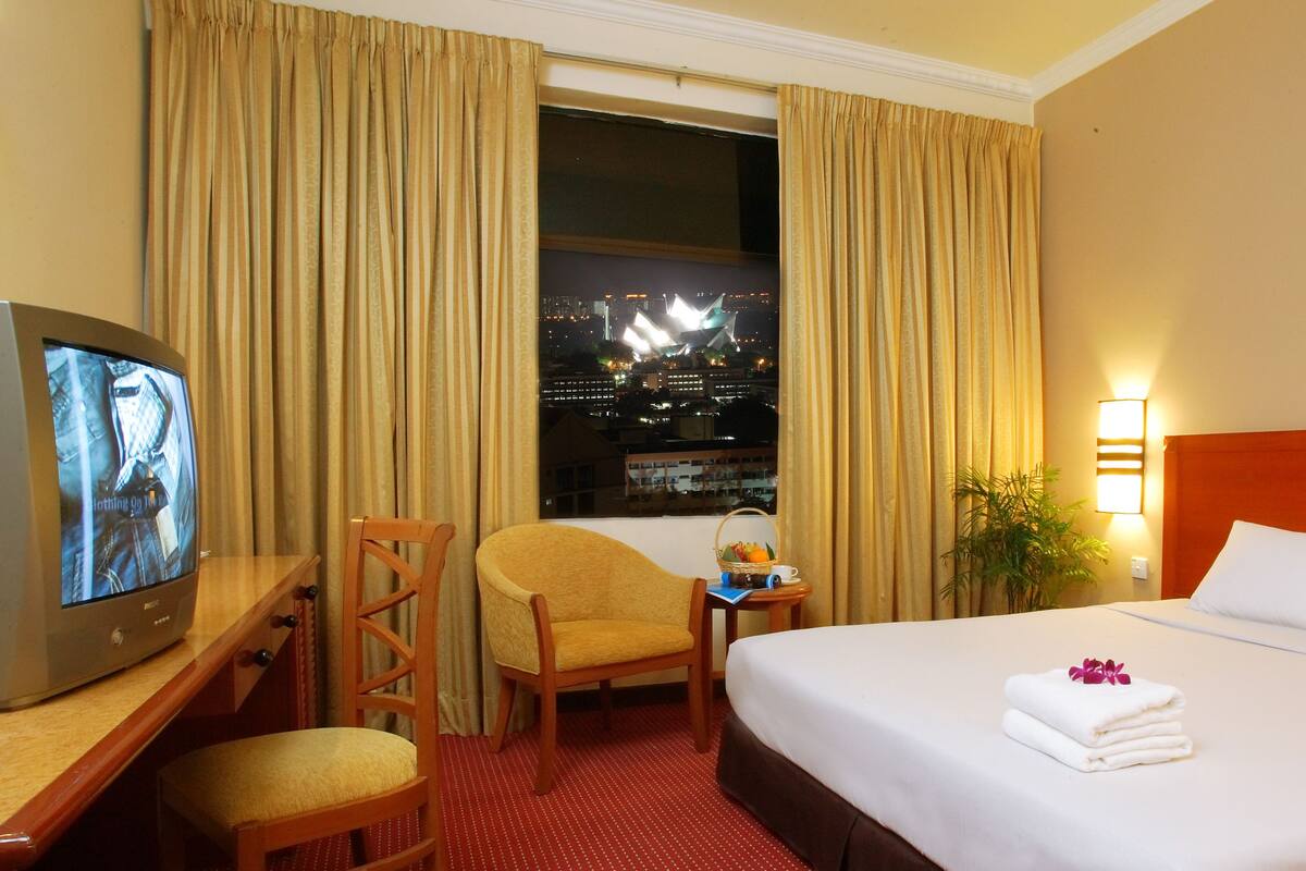 Une chambre d’hôtel comprenant un lit, un bureau avec une télévision, une chaise, une fenêtre avec des rideaux et un tableau au mur.