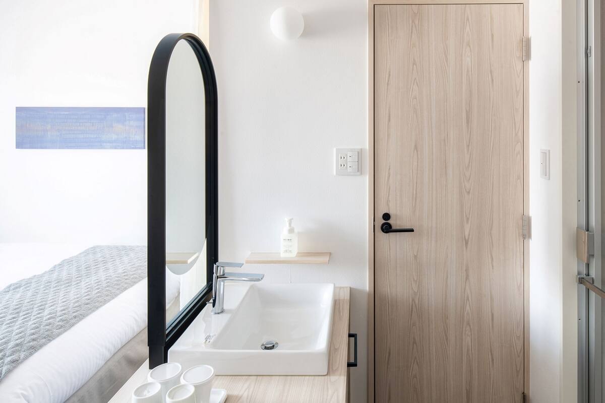 A modern bathroom with a white sink, a mirror, and a wooden door.