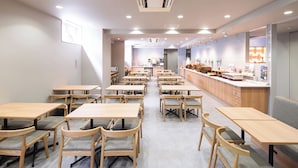 Un comedor amplio con varias mesas y sillas de madera, una encimera de cocina con diferentes utensilios, y un ambiente luminoso y bien iluminado.