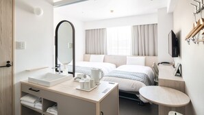 Habitación de hotel con un espejo grande, dos camas, una mesita de noche con hervidor, una mesa redonda pequeña y un televisor montado en la pared.