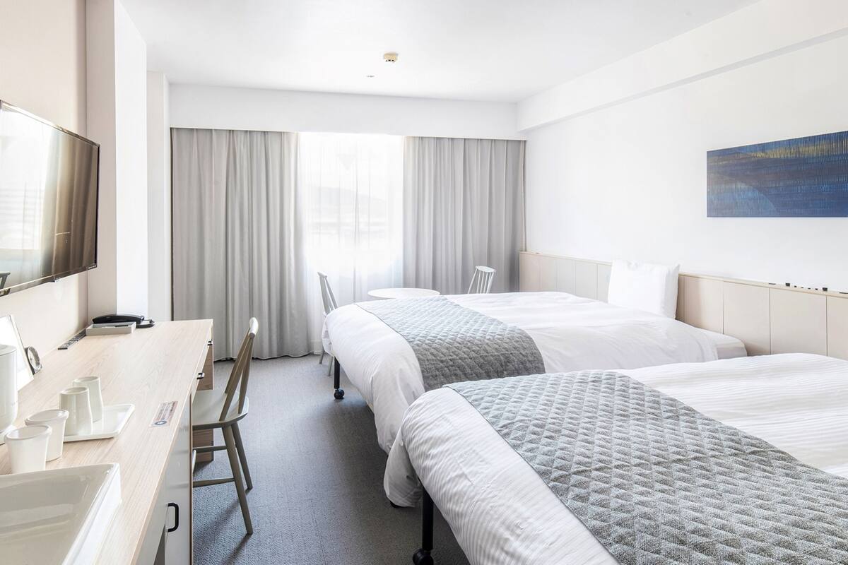 A hotel room with two beds, a desk with a coffee maker, a TV, and a painting on the wall.