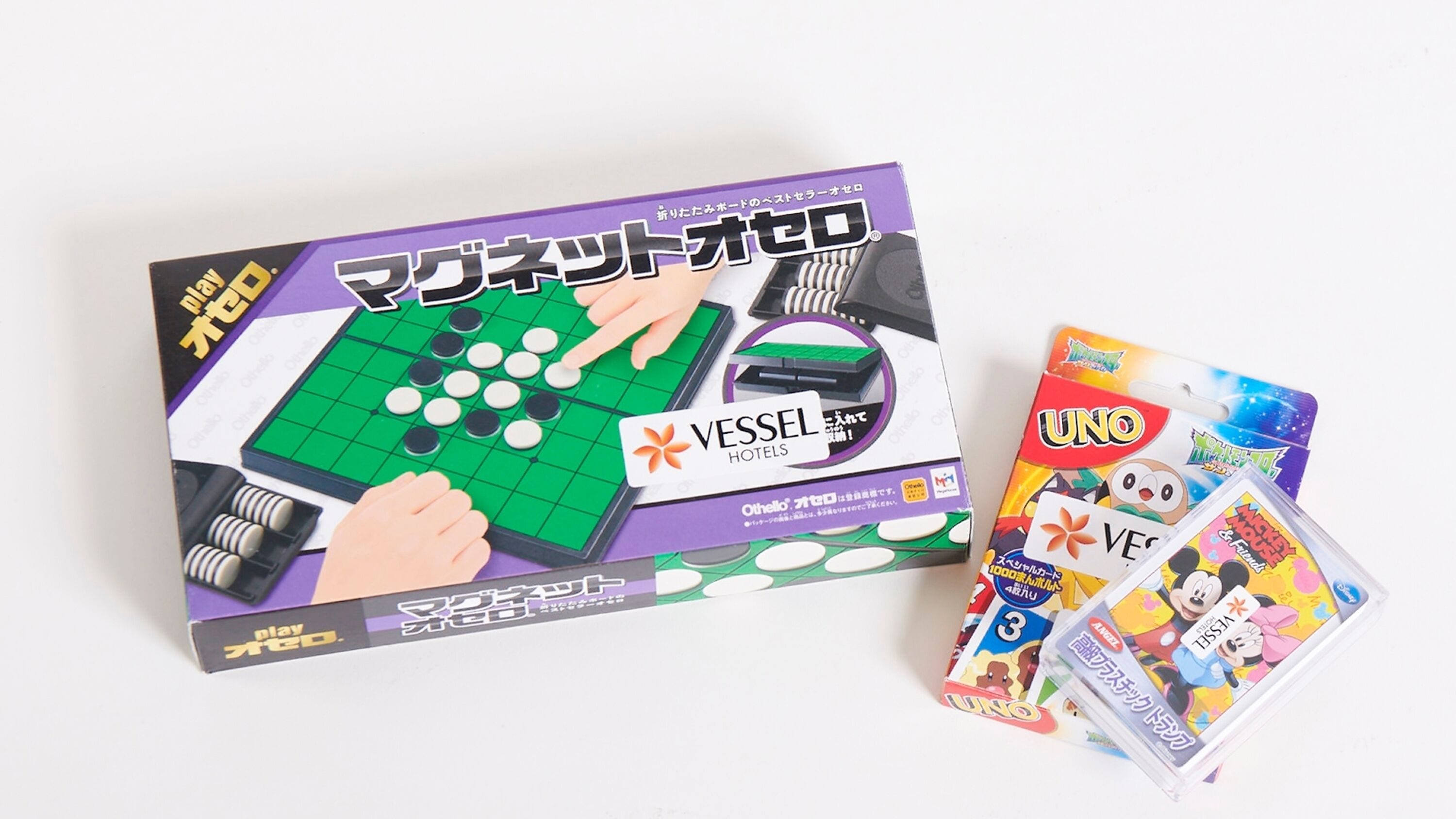 A board game with a green board and pieces, a box labeled "VESSEL HOTELS", and UNO cards.