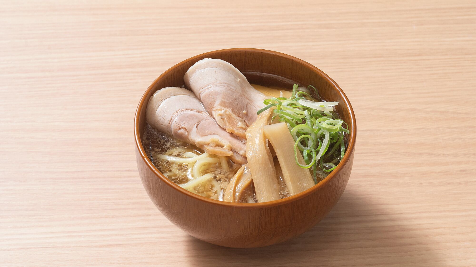 A bowl of ramen with noodles, sliced meat, and green onions on a wooden table.