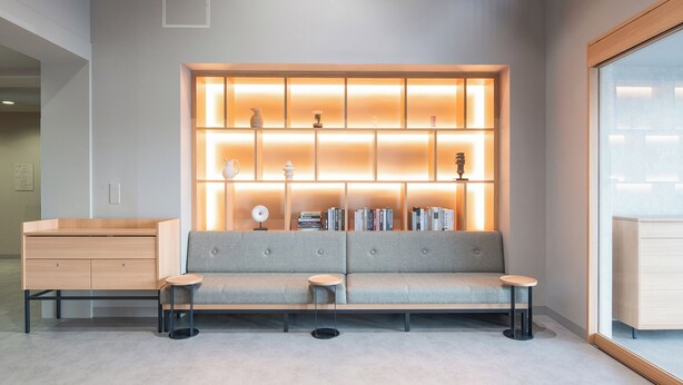 Una sala de estar moderna con un sofá gris, dos mesas auxiliares redondas y una estantería empotrada con libros y objetos decorativos.