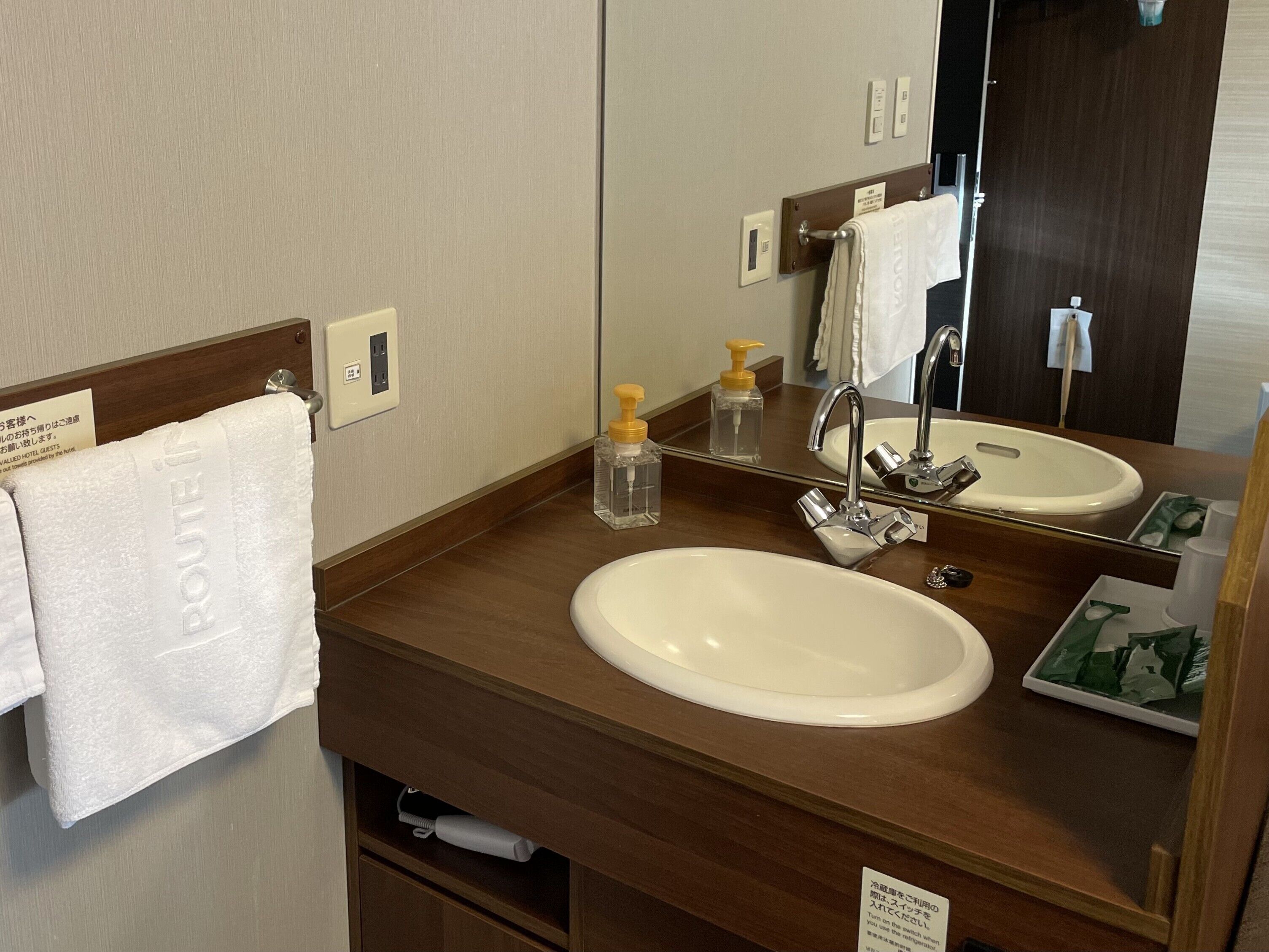 Un baño de hotel con lavamanos, espejo, toallero y dispensador de jabón.