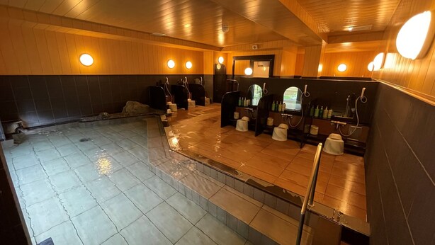 A public sauna with multiple benches, a stone floor, wooden walls, and round wall-mounted lights.