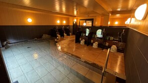 Eine öffentliche Sauna mit mehreren Bänken, Steinboden, Holzwänden und runden Wandleuchten.