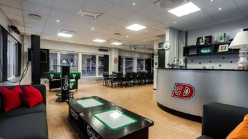 A modern lounge area with a pool table, sofas, and a bar area with a 3D logo.