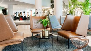 Een moderne lobby met lederen stoelen, een ronde tafel met een plant en een decoratieve metalen tafellamp.