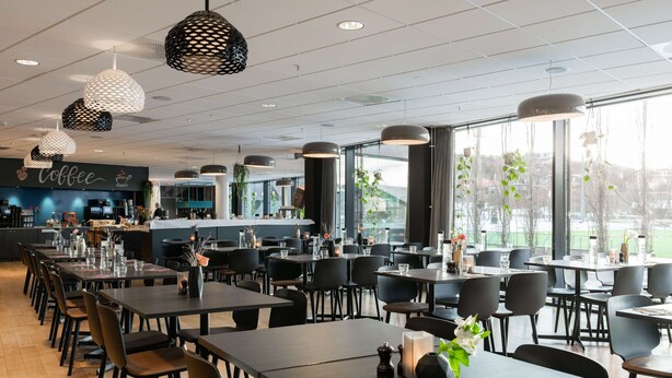 Een modern restaurant met een koffiebar, meerdere eettafels en hangende hanglampen.