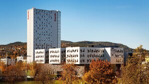 Een modern gebouw met een unieke geometrische gevel, omringd door herfstbomen en een heuvelachtig landschap op de achtergrond.