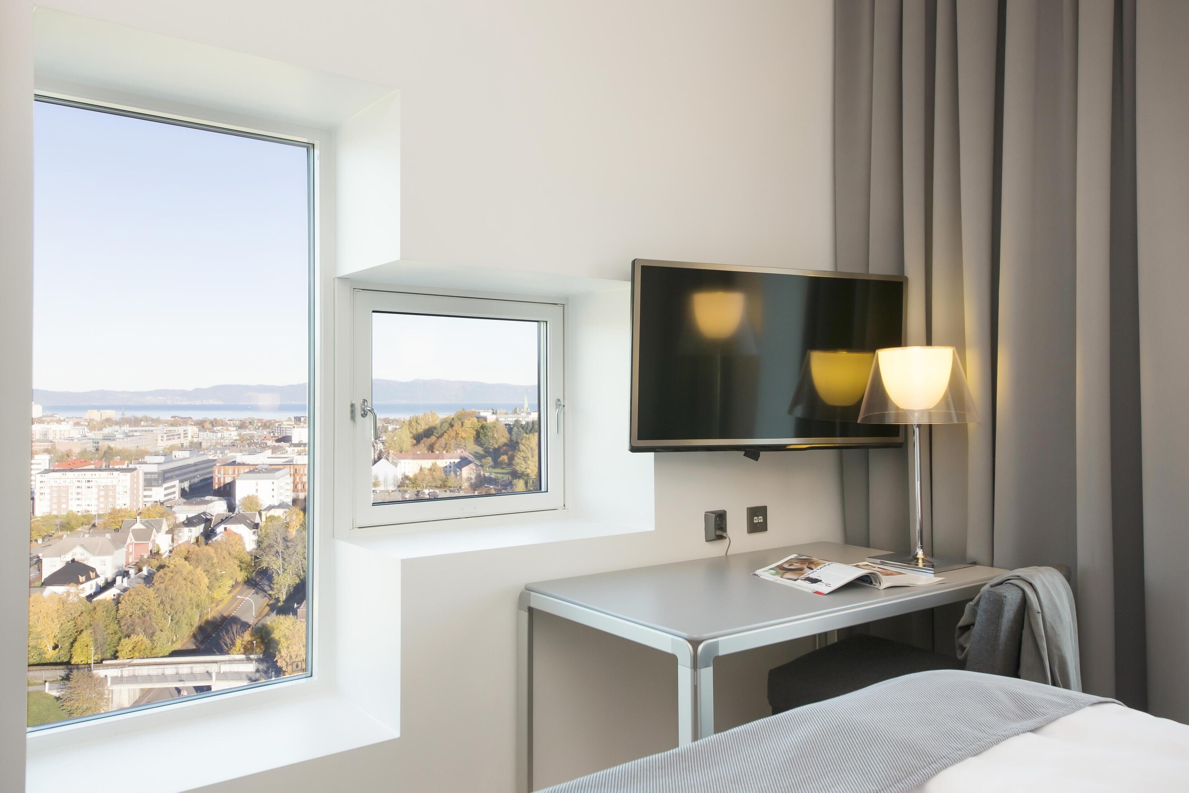 Habitación de hotel con cama, escritorio, televisión y ventana con vista a la ciudad.