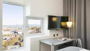 A hotel room with a bed, a desk, a TV, and a window with a city view.