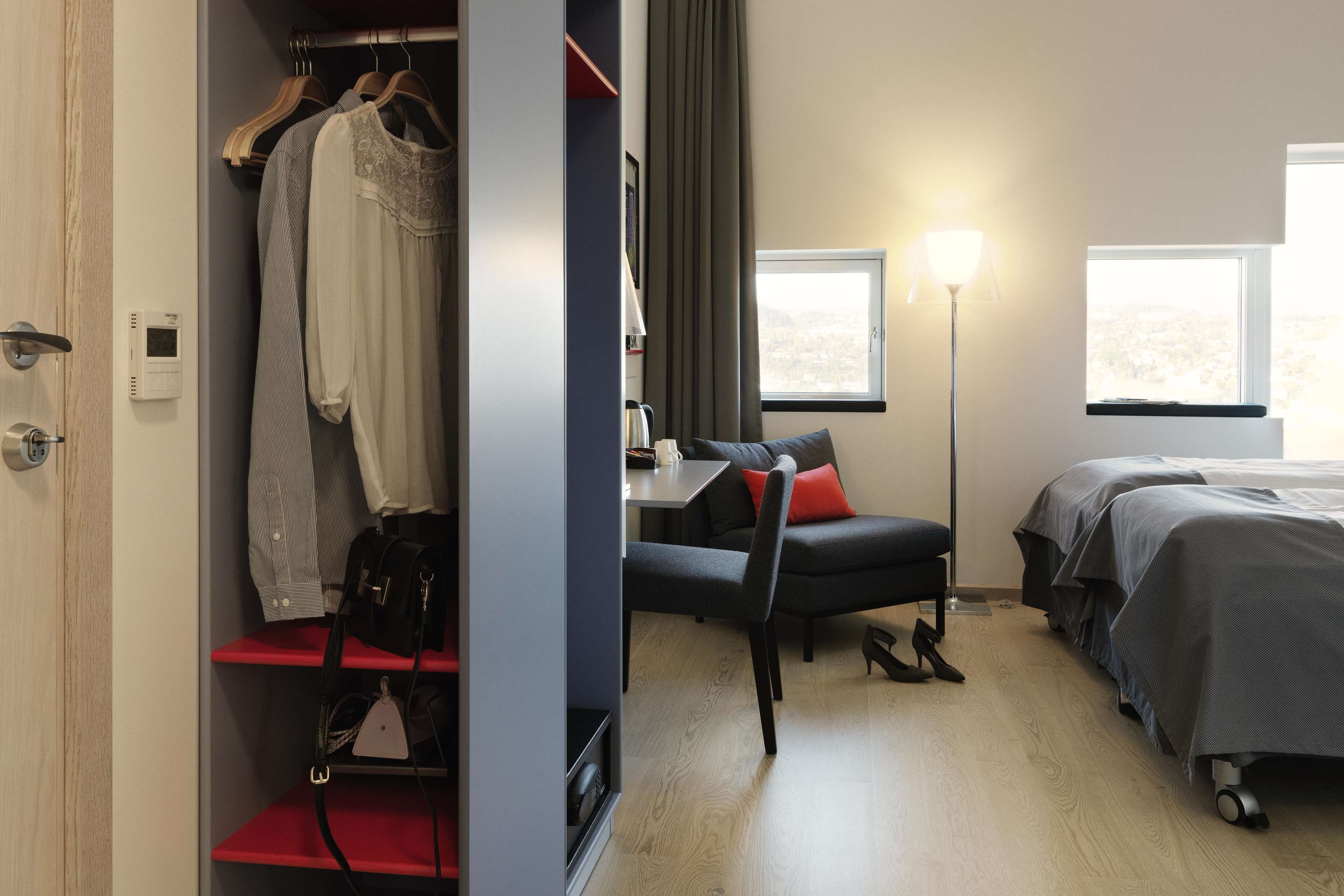 A hotel room with a bed, a desk with a chair, a wardrobe, and a window with a view.
