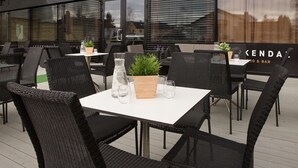 Een terras met rieten stoelen en tafels, een bloempot en een glazen pitcher.