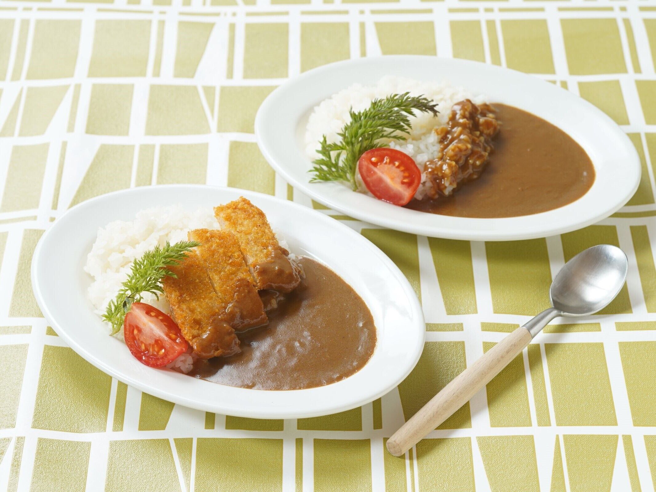 Two plates of food with rice, a breaded cutlet, and a brown sauce, garnished with a tomato slice and a sprig of dill, on a table with a geometric pattern.