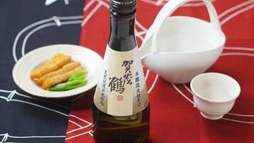 A bottle of sake with a label, a plate with food, and a white bowl on a tablecloth with a red and black pattern.