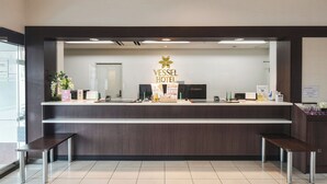 A reception desk at the Vessel Hotel with a modern design, a logo, and various amenities like a plant, a calendar, and a small table. - Vessel Hotel Higashi - Hiroshima (Higashihiroshima)