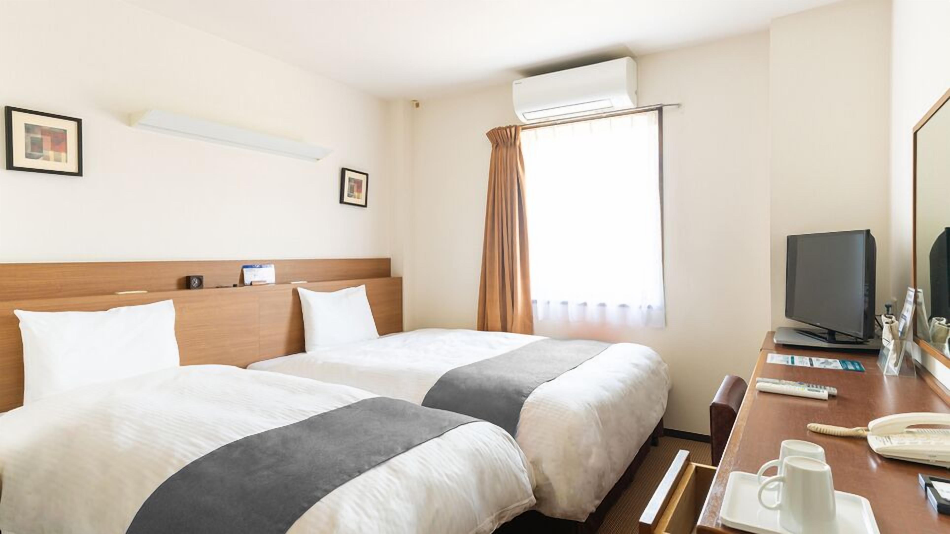 Una camera d'albergo con due letti, una scrivania con computer e telefono, e un condizionatore d'aria.