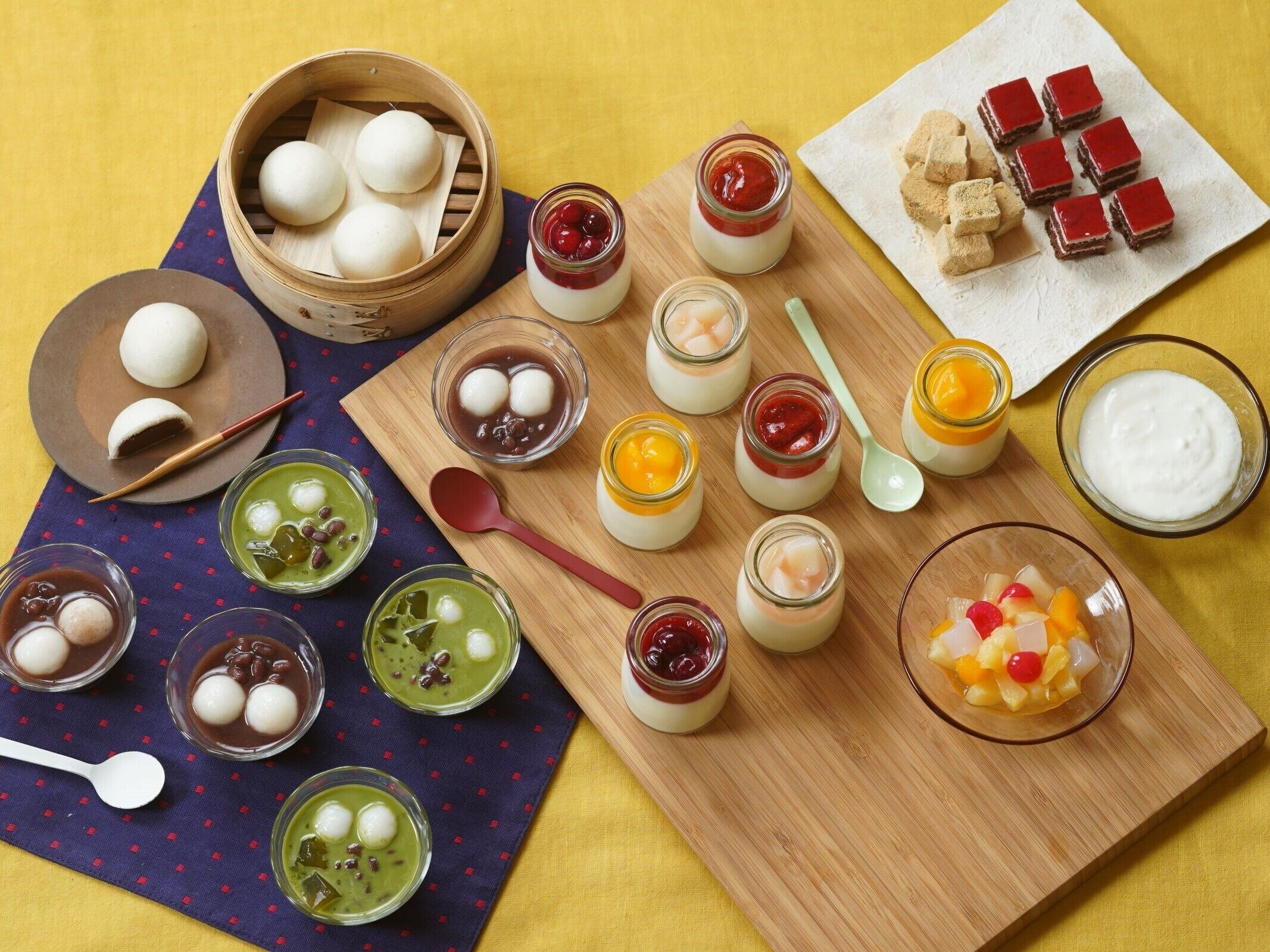 A variety of Asian desserts and snacks arranged on a wooden board and a plate, including steamed buns, jelly desserts, and sweet treats.