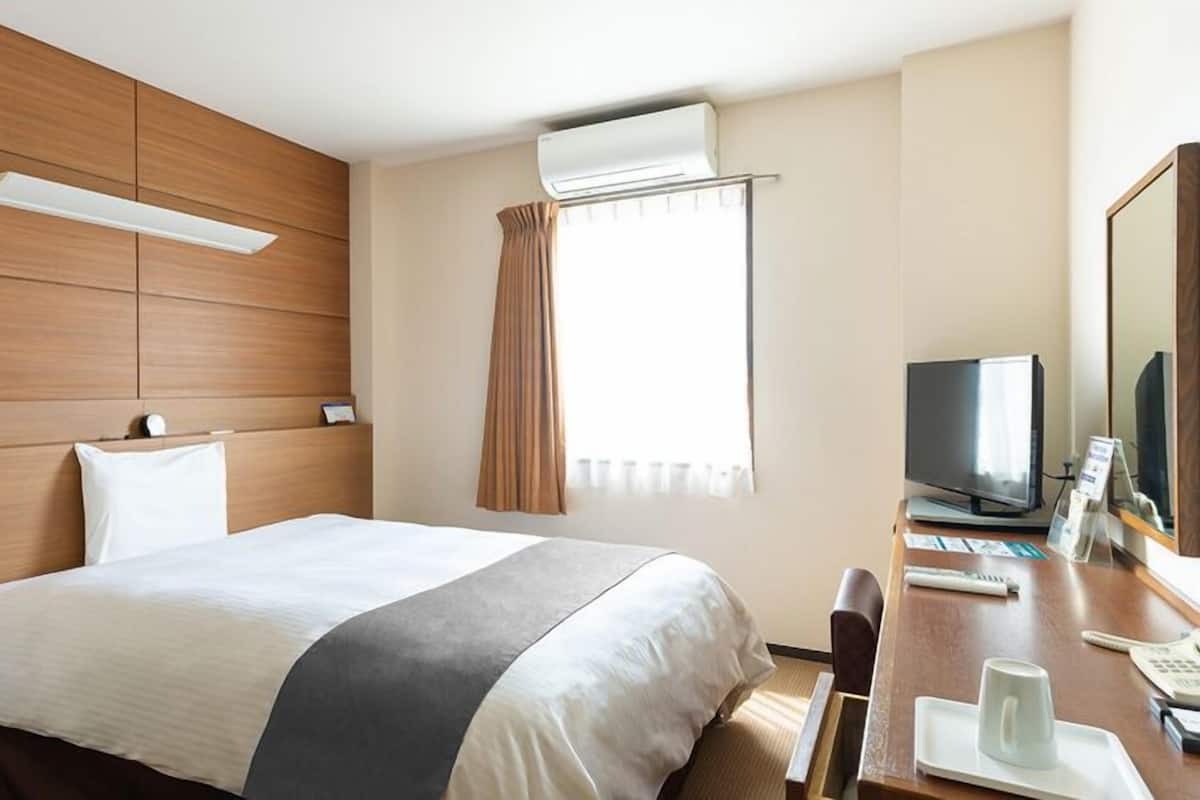 Una habitación de hotel con cama, escritorio con televisor, espejo y unidad de aire acondicionado.