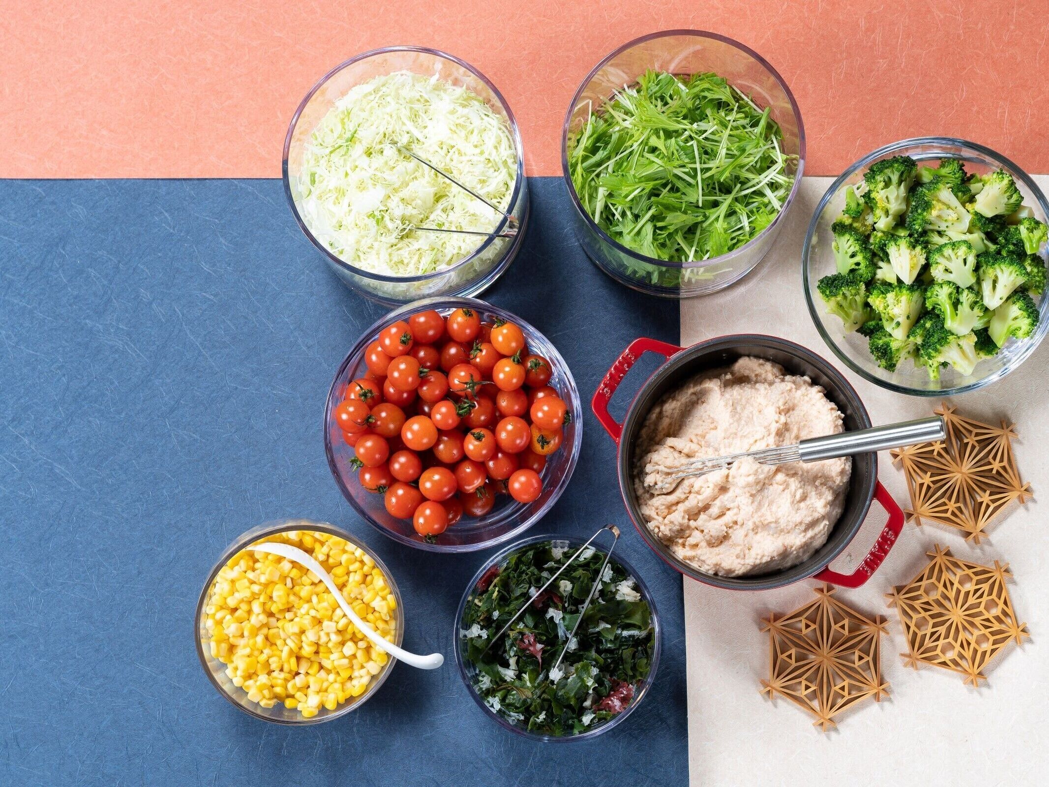 A variety of food items including shredded cabbage, green leafy vegetables, cherry tomatoes, corn, and a bowl of creamy dip.