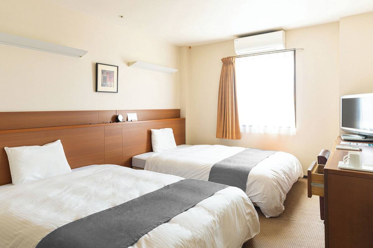 A hotel room with two beds, a wooden headboard, a flat-screen TV, and a window with curtains.