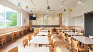 A spacious dining area with multiple tables and chairs, large windows offering a view of greenery, and a variety of pendant lights. - Vessel Hotel Higashi - Hiroshima (Higashihiroshima)
