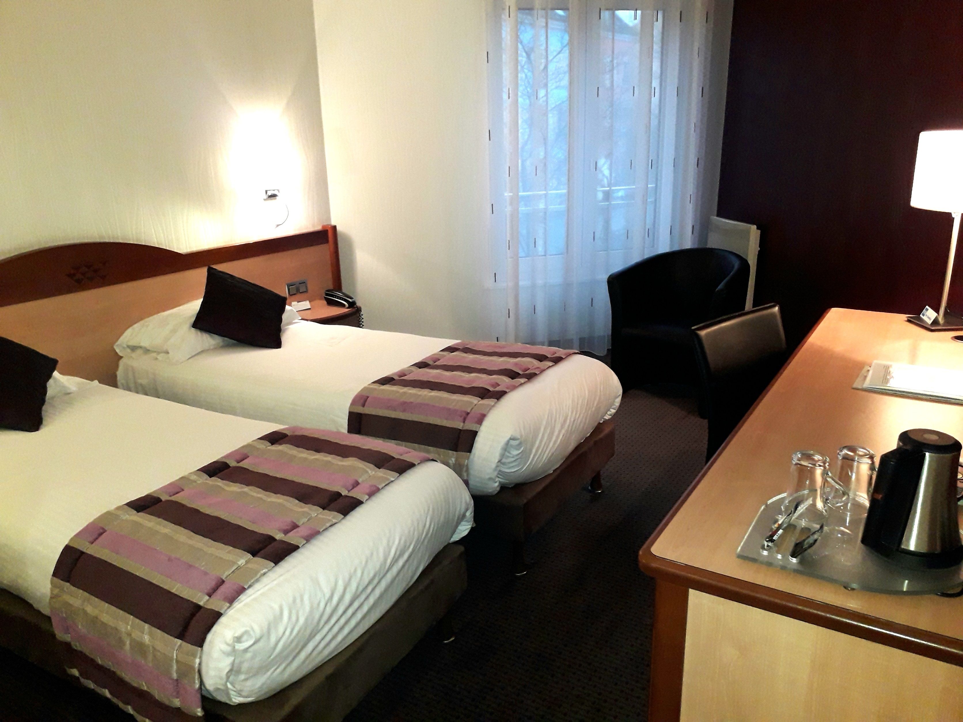 Habitación de hotel con dos camas, un escritorio, una silla y una ventana con cortinas.